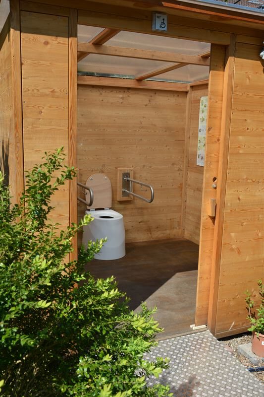 Toilette WALD barrierefrei nach DIN mit Ecodomeo. Blick in die Kabine. 90 cm links und rechts vom Sitz, Stützklappgriffe links und rechts.