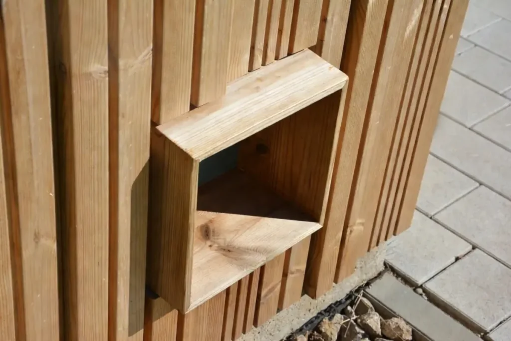 Detail der Fassade der Toilettenanlage KUBUS: vertikale massive Lärchenholzprofile mit Nut-und-Feder-Verbindung, abwechselnde Profilstärken erzeugen ein lebendiges Relief durch Licht- und Schatteneffekte, Nahaufnahme des Holzes mit natürlicher Maserung und Tiefe