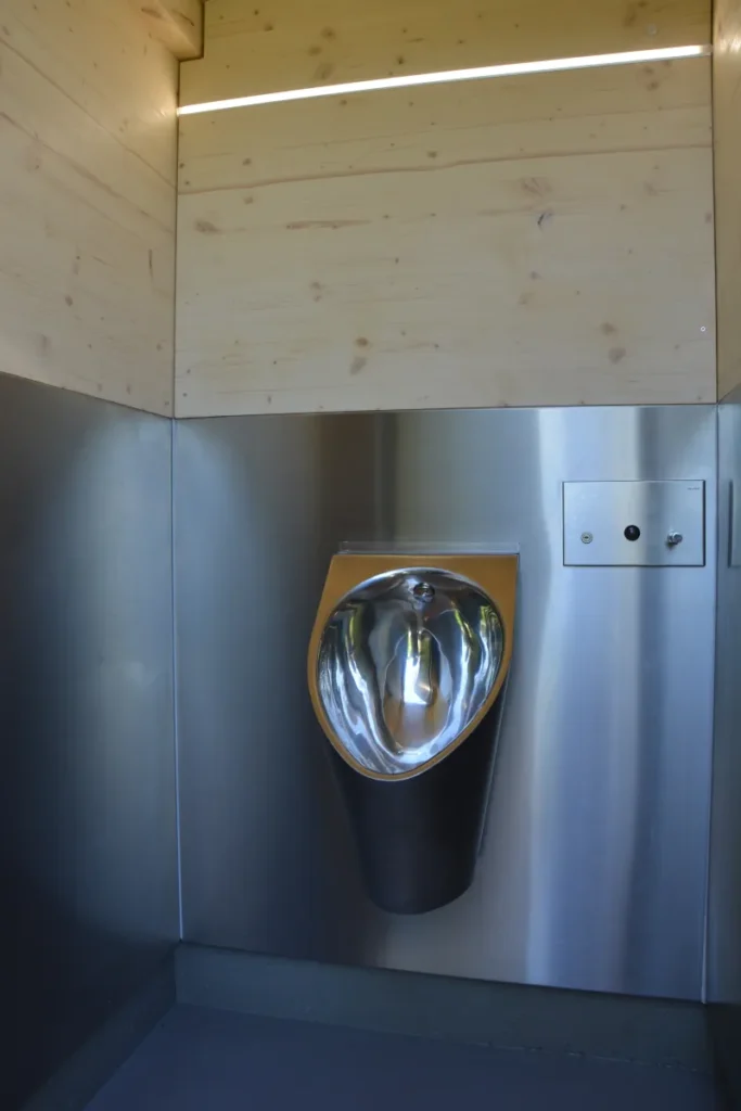 Wasserloses Edelstahl-Urinal für Herren in der öffentlichen Toilettenanlage KUBUS: in separater Kabine mit abschließbarer Tür, wandintegrierter und vandalismussicherer Handgelspender, LED-Indirektbeleuchtung, hygienisch, wassersparend und umweltfreundlich – die separate Raumaufteilung ermöglicht parallele Nutzung von Urinal und Toilette