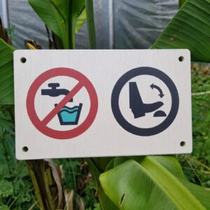 Holzschild aus lasiertem Sperrholz mit zwei Symbolen: links „Kein Trinkwasser“ (durchgestrichener Wasserhahn über Becher) und rechts Symbol für Fußpumpe – Befestigungslöcher an den vier Ecken